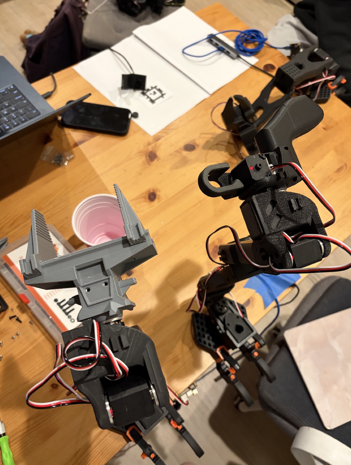 The original pointed gripper claws beside the redesigned parallel rail-based claw, on a workbench